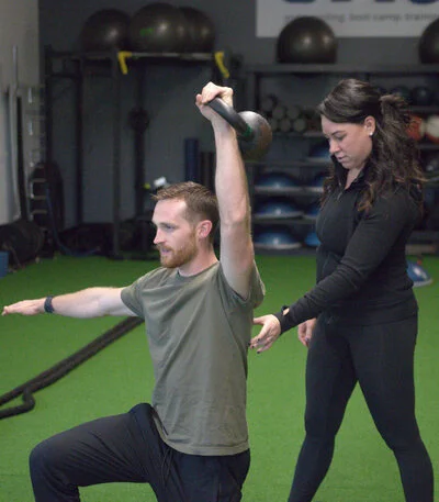 a young man working out with kettle bells as Bree helps perfect his form